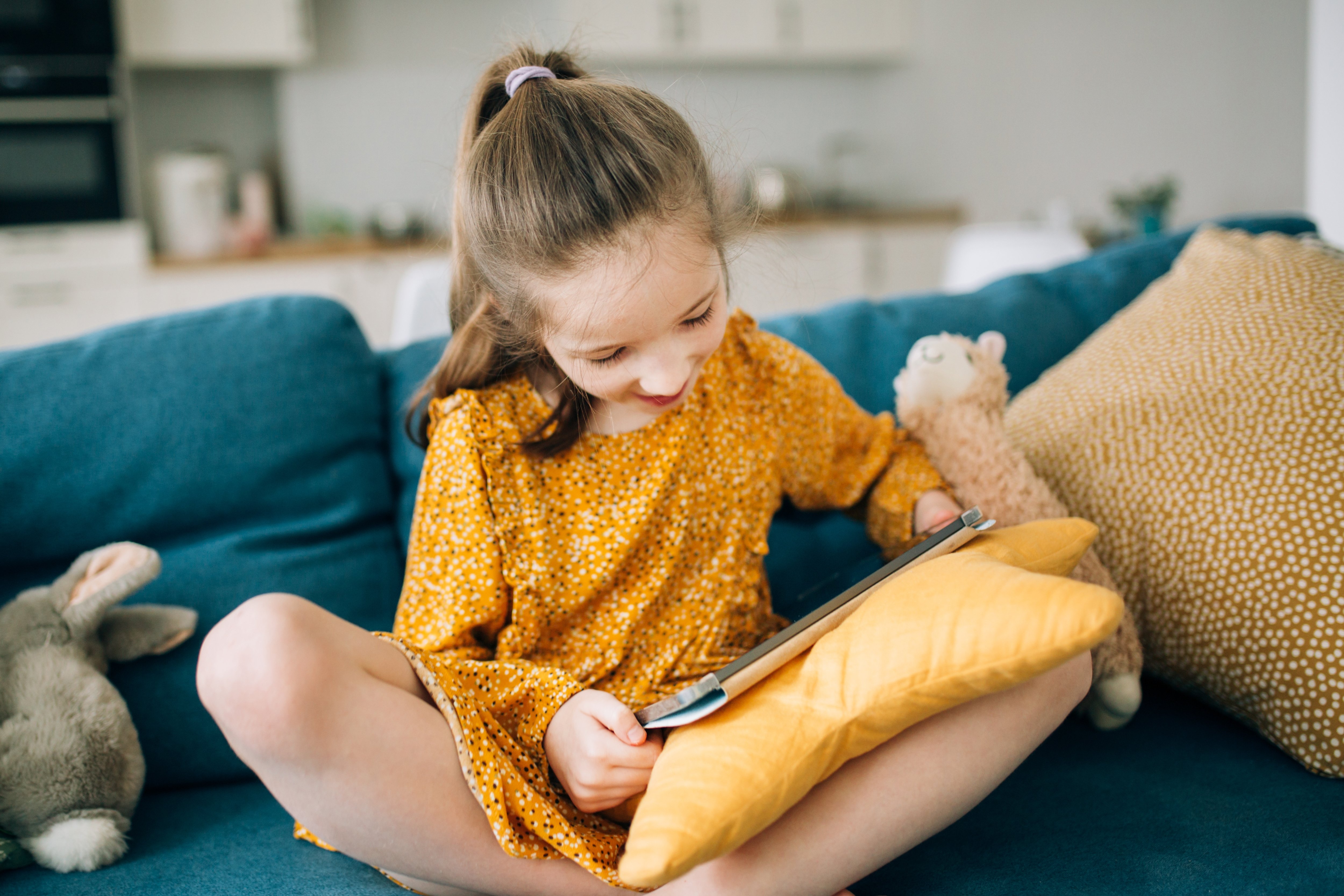 a-girls-is-sitting-on-a-sofa-with-tablet-and-toys-SCK855W